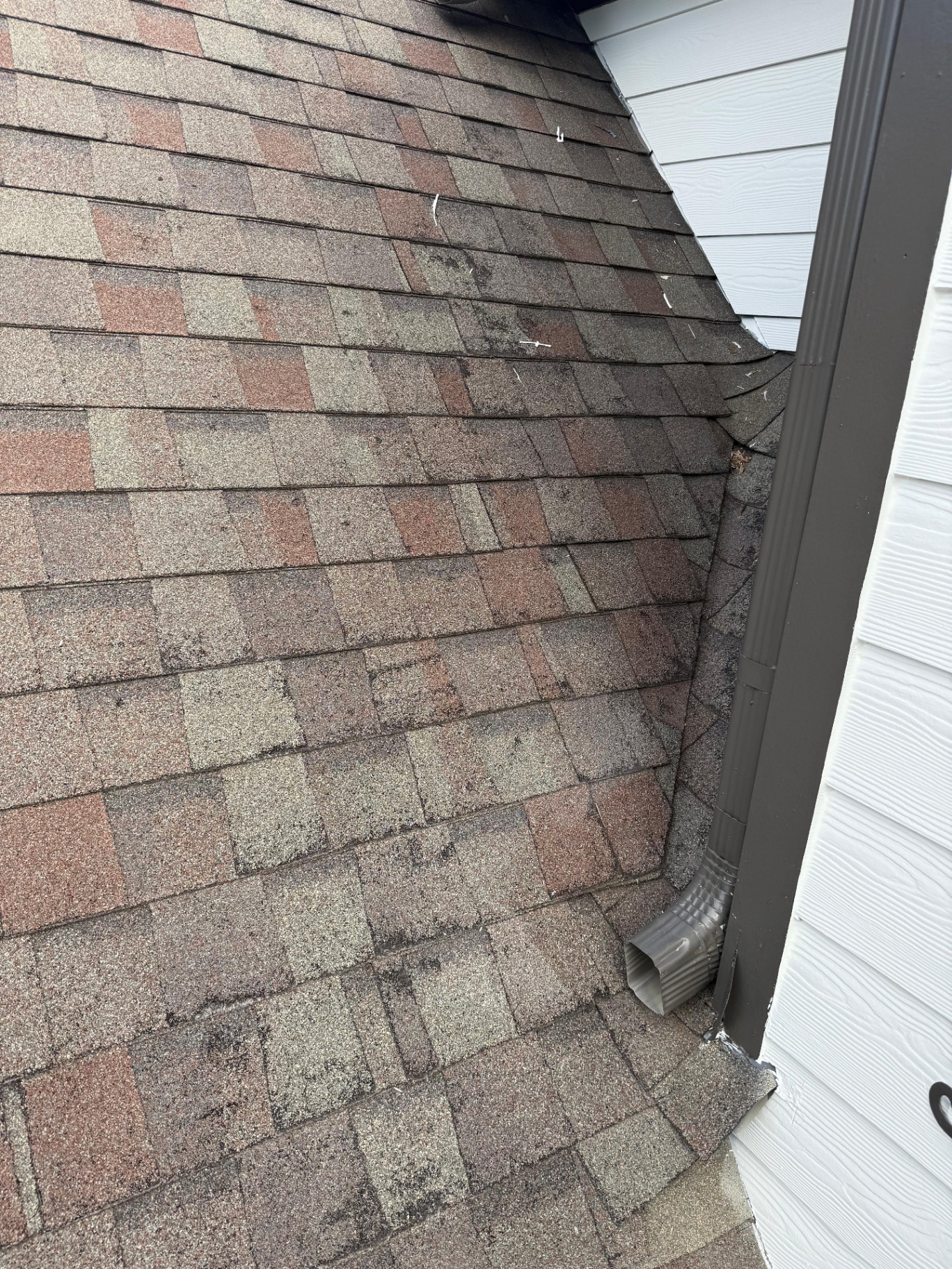 Asphalt shingles showing granule loss and weathering patterns concentrated along a roof valley line — visible signature of hail damage that channels into the valley after impact