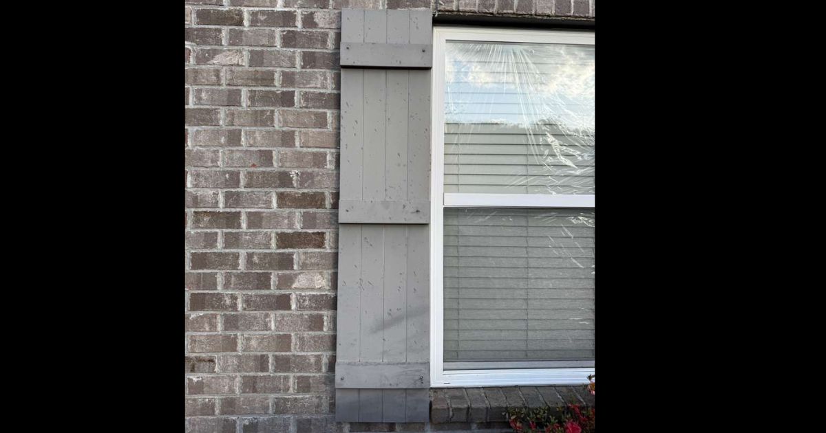 Painted wood shutters on a brick home showing multiple hail impact dents and dimpling across the surface — evidence of hail of damaging size that adjusters use to corroborate roof damage claims